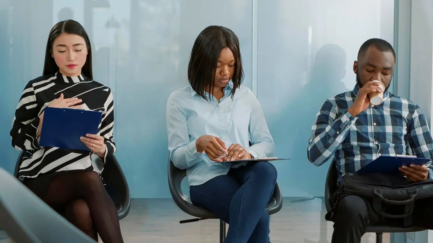 Eine vielfältige Gruppe von Bewerberinnen und Bewerbern steht in der Schlange, um das HR-Team zu treffen und über Karrieremöglichkeiten zu sprechen. In der Bürolobby sitzen nervöse Personen, die erwarten, an einem Vorstellungsgespräch teilzunehmen.